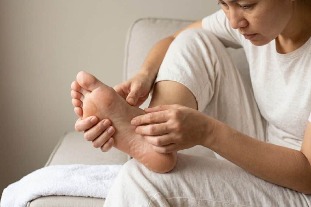 A person sitting down and carefully examining the sole of their own foot with their hands during a routine home health and skin check.